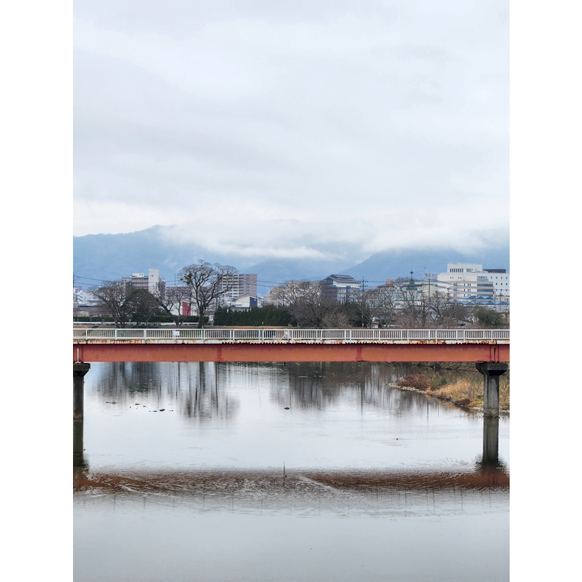 川の近くから見る山々に雲がかかっている様子の写真